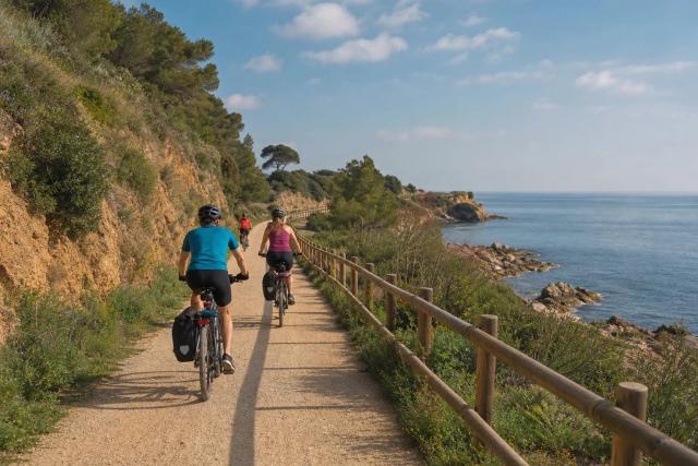 Cyclists riding side by side on a flat, traffic-free greenway on an old railway path outside Barcelona