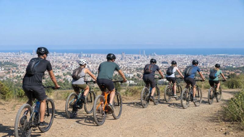 Small group of cyclists riding a quiet coastal road above a rocky cove on a clear morning