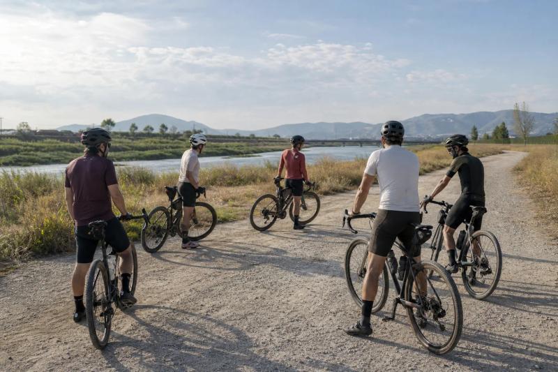 Group of first-time gravel riders pausing on a compacted riverside path near Barcelona
