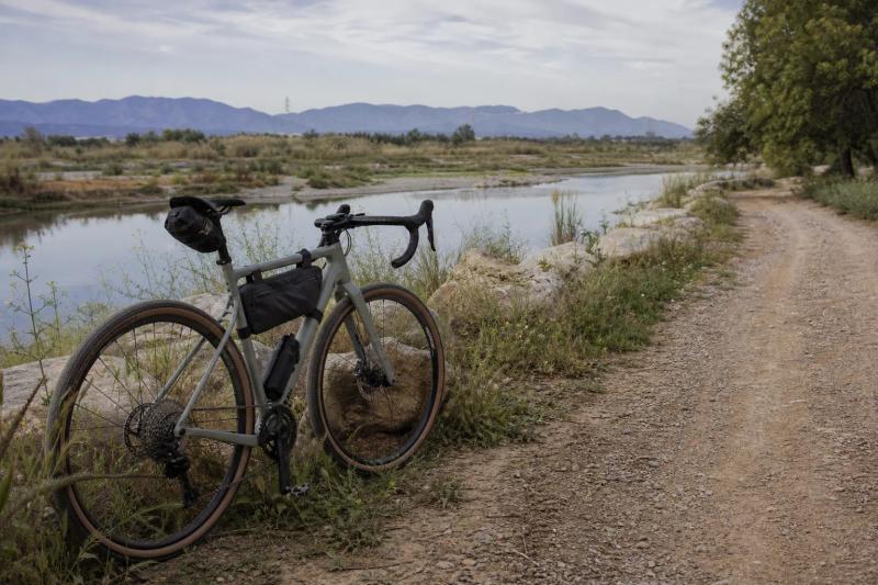 Gravel bike resting beside a calm river with open tracks ahead near Barcelona