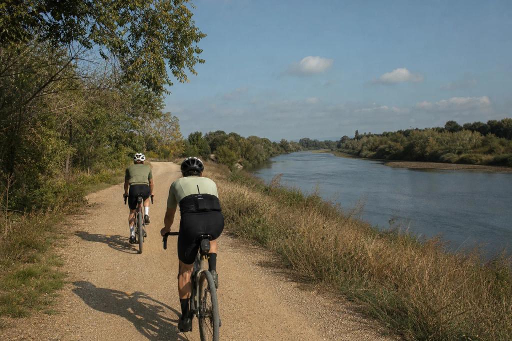 Riders on gravel bikes following a wide riverside track out of Barcelona