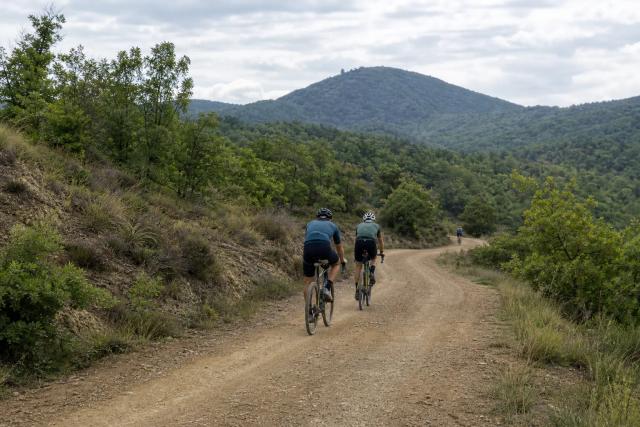 Gravel rider climbing a stony track beside a forested extinct volcano in the Garrotxa